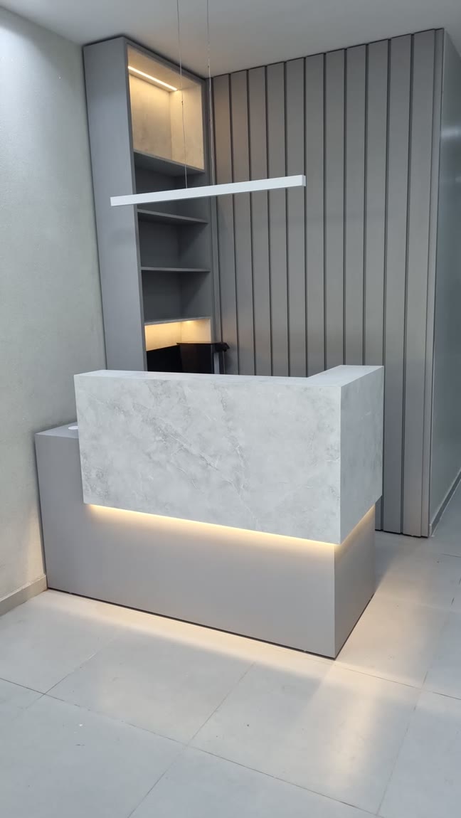 Balcão de recepção revestido em pedra marmorizada, com fita de LED por baixo e nichos iluminados atrás.