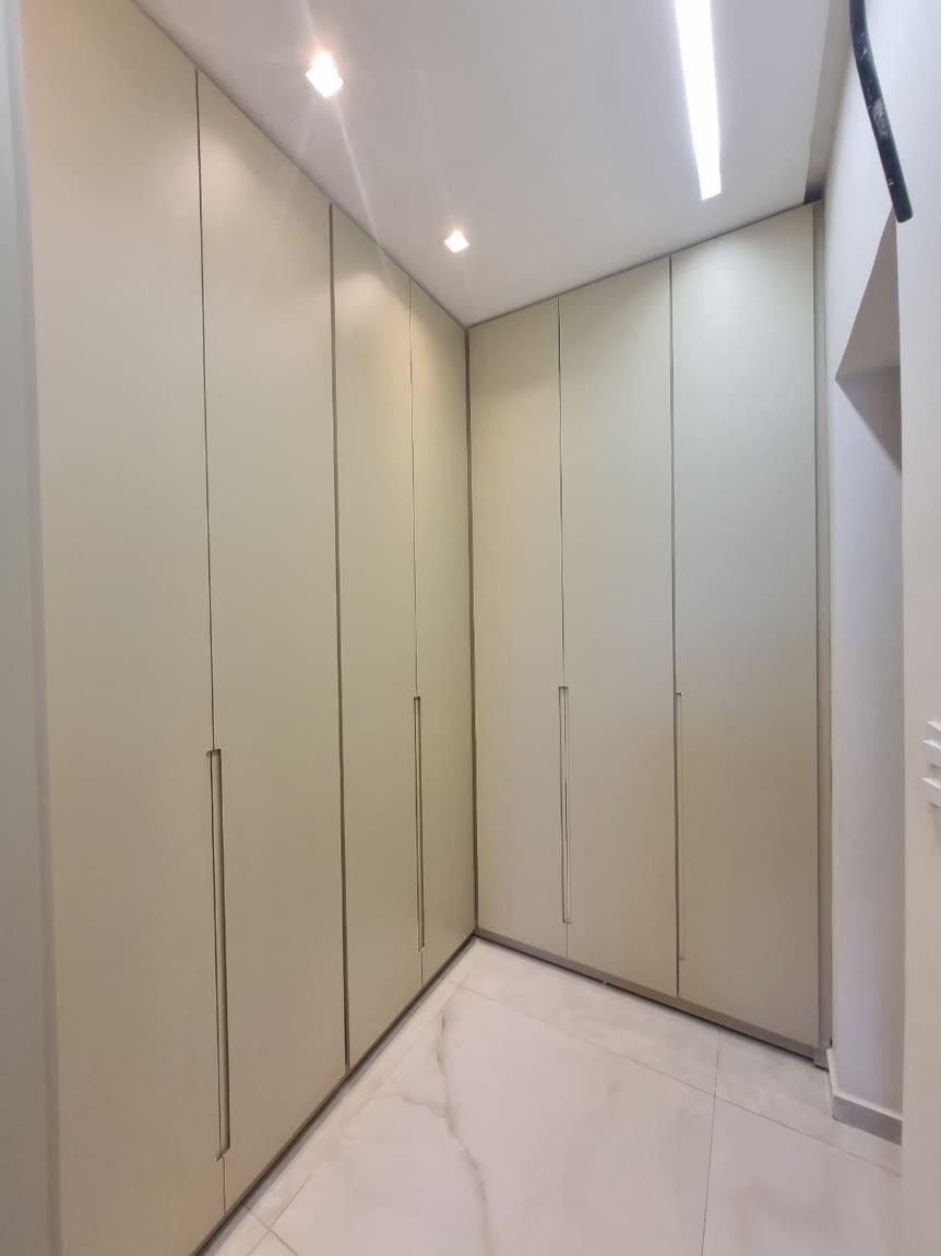 Closet fechado com portas altas em bege e puxador perfil embutido, ocupando duas paredes.