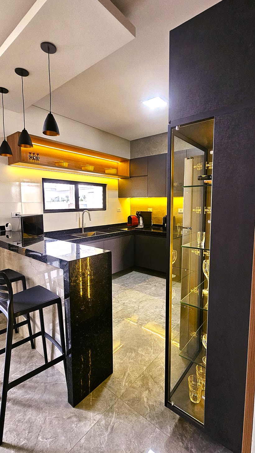 Cozinha com bancada de granito preto, banquetas e adega de vidro iluminada por dentro.