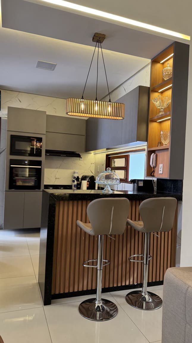 Cozinha com bancada de refeição em ripado de madeira, tampo de granito preto, banquetas altas e nichos de vidro iluminados.