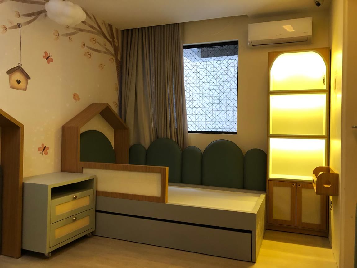 Quarto infantil com cabeceira em formato de casinha, estofados verdes arredondados e nicho iluminado em amarelo.
