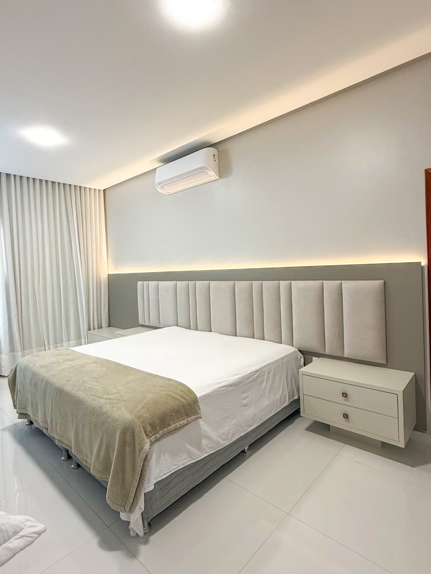 Quarto com cabeceira larga estofada e fita de LED acesa correndo por cima dela.