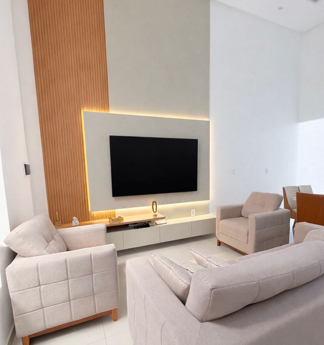 Sala com painel de TV em laca clara, luz de LED por trás do painel e ripado de madeira ao lado.